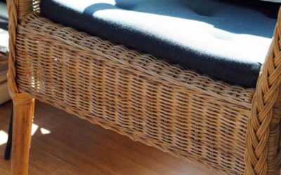 Un fauteuil en rotin avec coussin noir posé sur un sol en bois