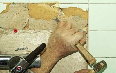 Une main tient un burin et un marteau pour enlever du carrelage